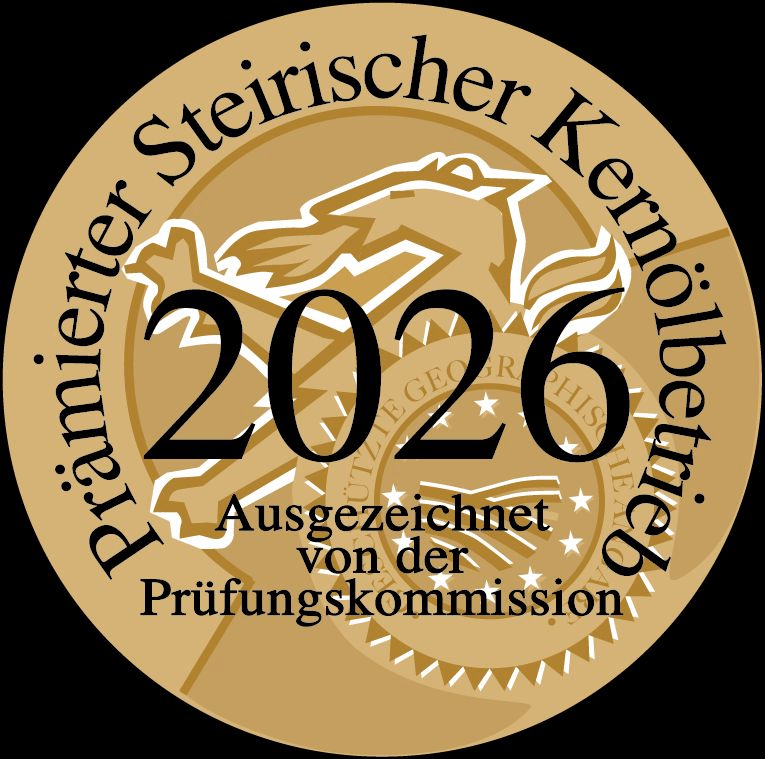 Ein goldener runder Abzeichen mit den Worten 'Prämierter Steirischer Kernölbetrieb 2026'. Es zeigt ein stilisiertes Bild eines Vogels und die Zahl '2026'. Das Abzeichen wird von der Prüfungskommission verliehen.