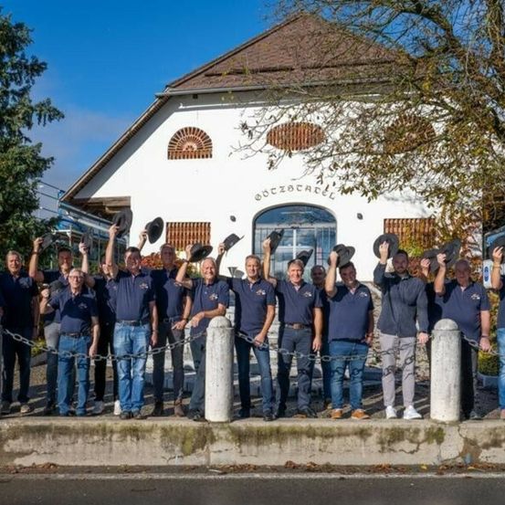 Eine Gruppe von Männern in passenden Uniformen steht vor einem weißen Gebäude, hält Hüte und posiert für ein Foto.