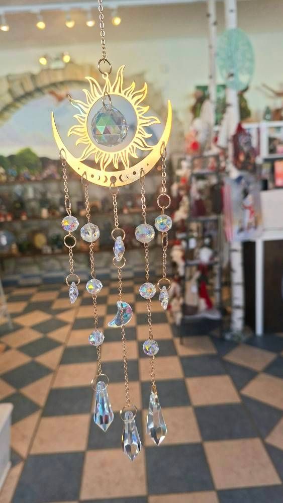 Eine goldene, sonnenförmige Windglocke mit Kristallen, die in einem Geschäft hängt. Der Laden hat einen Schachbrettboden.