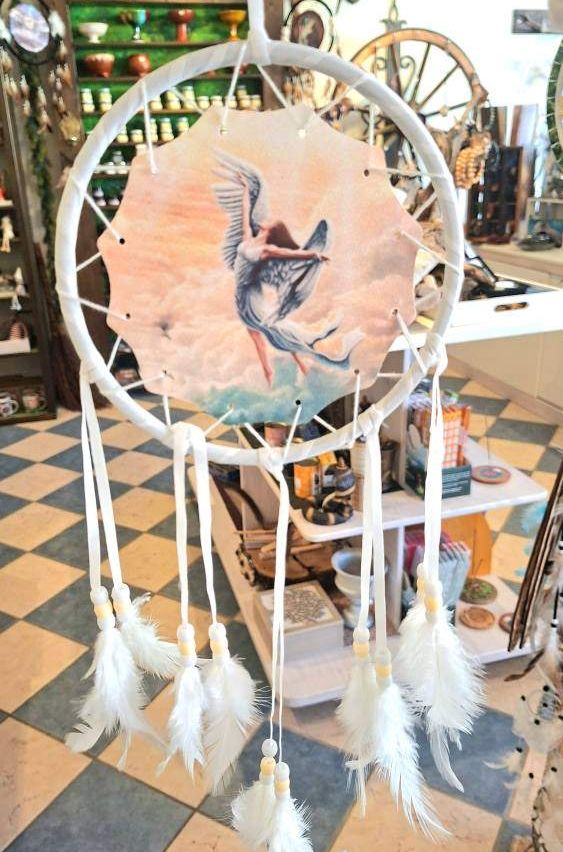 Ein Traumfänger mit weißen Federn und einem kreisförmigen Rahmen ist in einem Geschäft ausgestellt. Ein Engel fliegt über den Wolken.