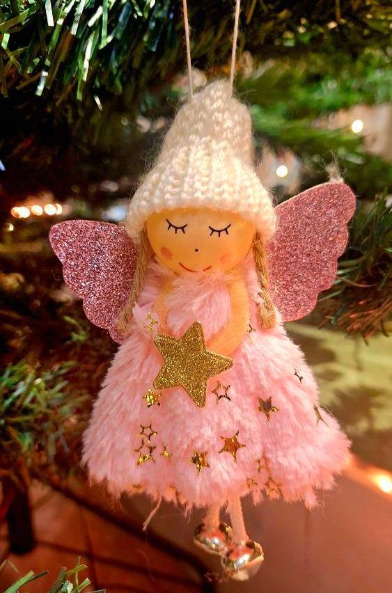 Eine rosa Fee mit weißer Mütze und rosa Kleid hängt an einem Weihnachtsbaum. Die Puppe hat rosa glitzernde Flügel und Sterne und hält einen goldenen Stern.