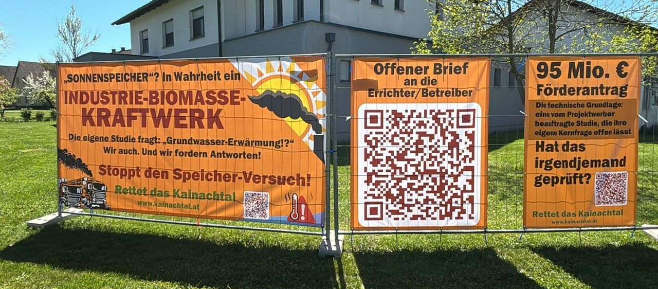 Zwei Banner an einem Zaun vor einem Gebäude, eines sagt 'Biomasse-Netzwerk' und das andere hat einen QR-Code.