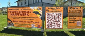Zwei Banner an einem Zaun vor einem Gebäude, eines sagt 'Biomasse-Netzwerk' und das andere hat einen QR-Code.