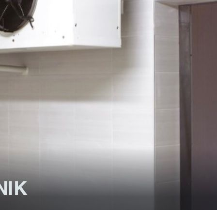 Eine gewerbliche Kühleinheit, die an der Wand über einer gefliesten Wand montiert ist, mit einer geschlossenen Tür auf der rechten Seite. Die Einheit hat einen schwarzen Lüfter und eine Rohrleitung an der Vorderseite. Das Bild hat einen Wasserzeichen, der 'ILTECHNIK' lautet.