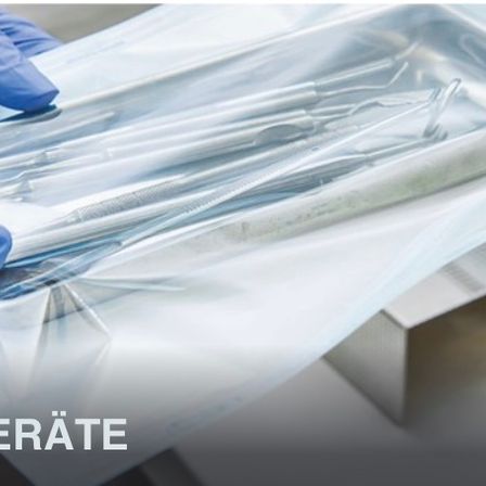 Eine Person in blauen Handschuhen hält einen durchsichtigen Plastikbehälter mit Zahninstrumenten. Der Behälter ist transparent und das Wort 'KUUMGERAATE' ist in schwarz am Boden gedruckt.