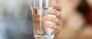 Eine Person hält ein Glas Wasser, möglicherweise kurz davor, es zu trinken. Das Glas ist klar, und das Wasser darin ist sauber.