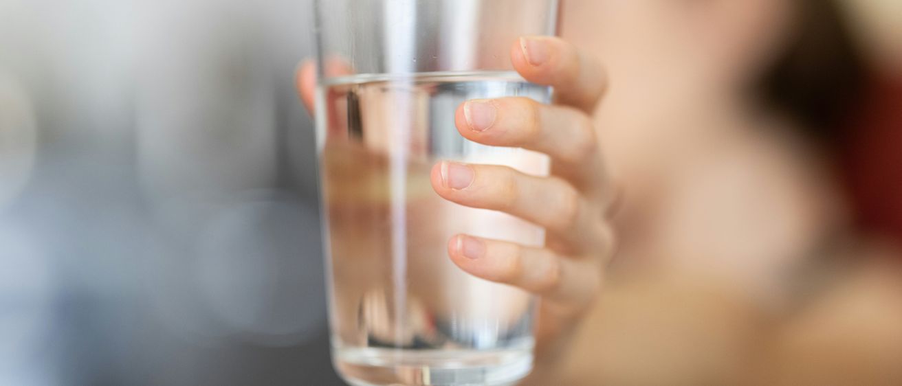Eine Person hält ein Glas Wasser, möglicherweise kurz davor, es zu trinken. Das Glas ist klar, und das Wasser darin ist sauber.