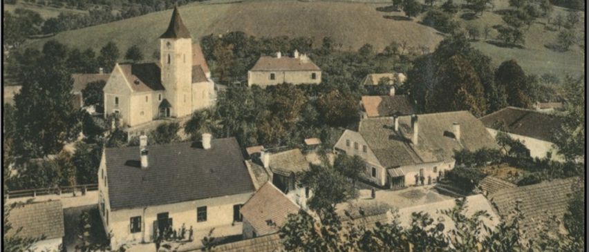 Ein altes Foto zeigt das Dorf Stossing mit mehreren Gebäuden, einer Kirche und einem Turm, umgeben von grünen Feldern und Bäumen.