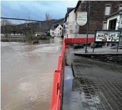 Eine überflutete Straße mit Gebäuden an der Seite, einer Brücke in der Ferne und roten Barrieren auf dem Bürgersteig.
