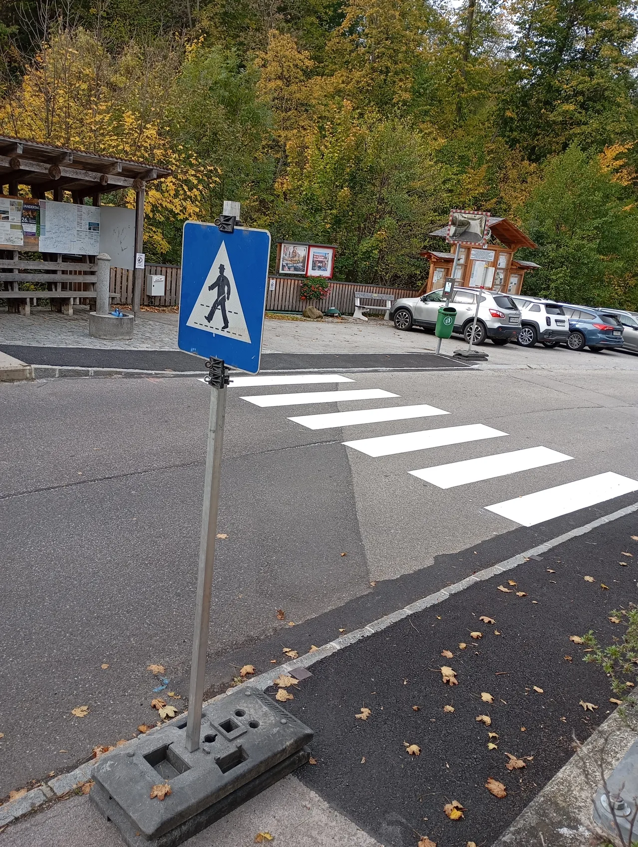 Ein Fußgängerübergangsschild befindet sich am Straßenrand mit weißen Streifen auf dem Bürgersteig.