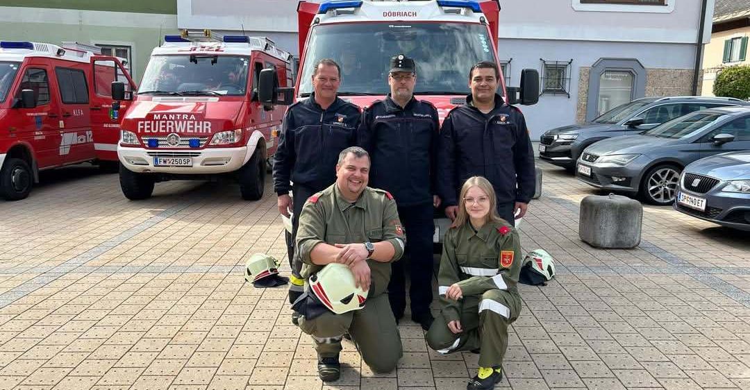 Eine Gruppe Feuerwehrleute in grünen Uniformen posiert vor einem Feuerwehrwagen mit der Aufschrift Dobřiach.