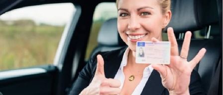 Eine Frau lächelt und gibt ein Daumen hoch, während sie einen Führerschein der Europäischen Union hält. Sie sitzt in einem Auto.