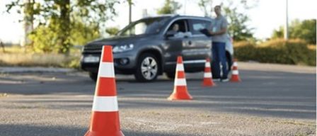 Eine Person steht neben einem geparkten SUV mit Kegel davor, wahrscheinlich führt sie einen Fahrtest durch.