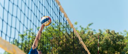 Ein Mann in einem blauen Shirt spielt Beachvolleyball und schlägt den Ball über das Netz.