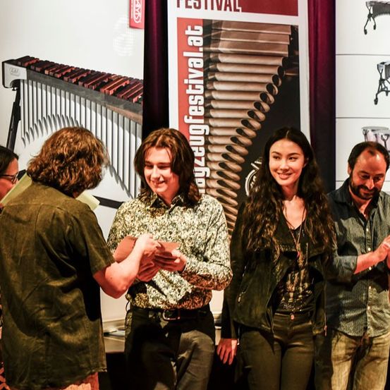 Eine Gruppe von Menschen steht auf der Bühne und klatscht, vor einem Banner des Zagreb Festivals im Hintergrund. Eine Frau hält eine Urkunde und ein Mann eine Plakette.