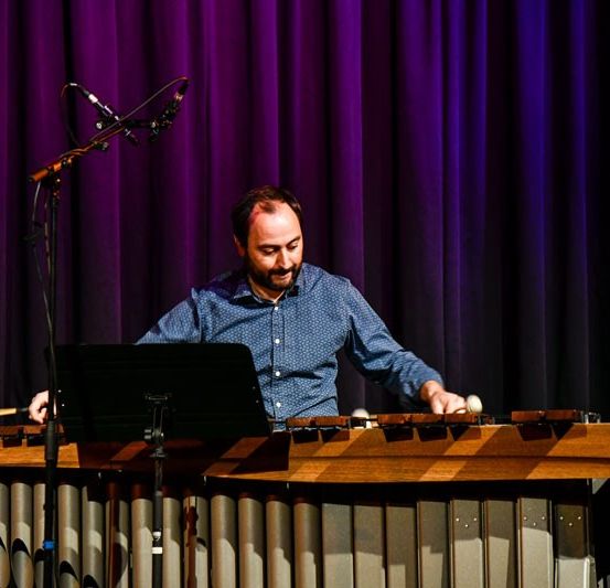 Ein Mann spielt eine Marimba auf der Bühne vor einem Mikrofon und mit lila Vorhängen im Hintergrund.