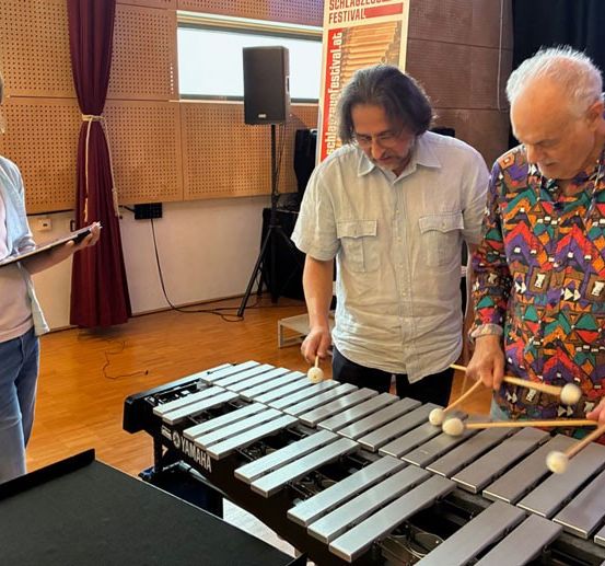 Drei Musiker spielen ein Yamaha-Xylophon in einem Studio. Eine Frau hält ein Tablet, und zwei Männer schauen sie an. Dahinter steht ein Lautsprecher und ein Fenster.