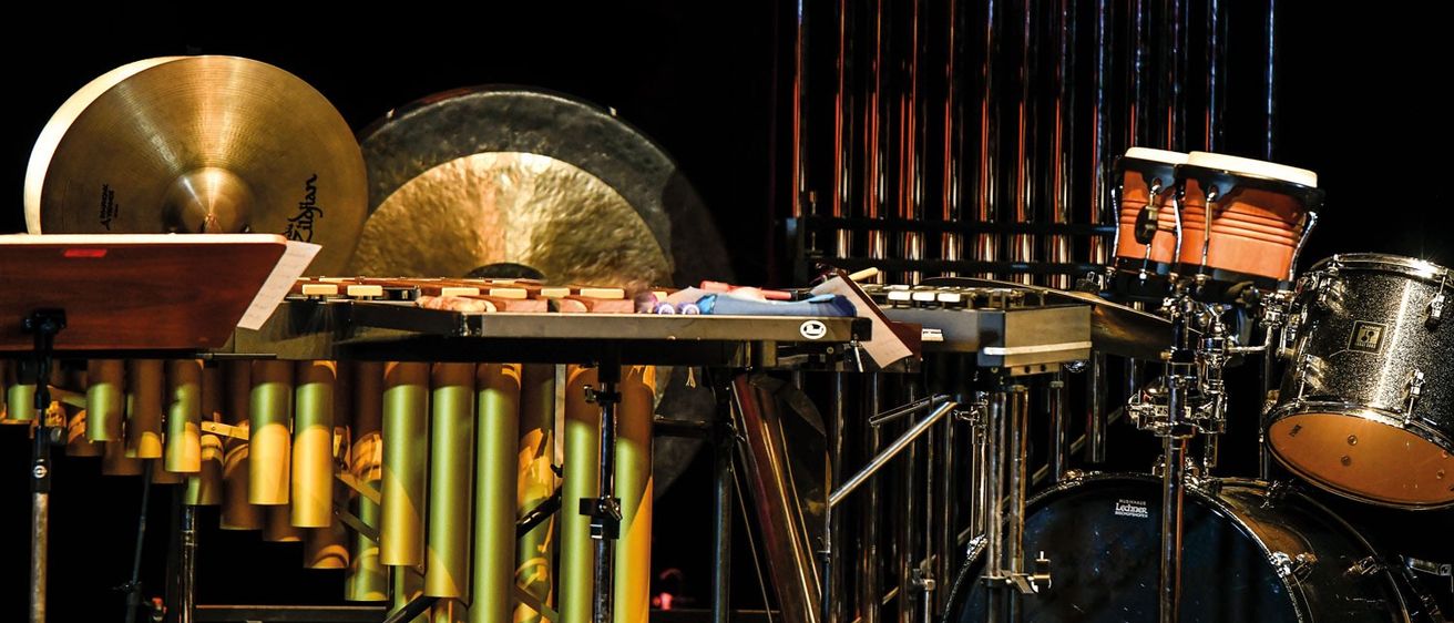 Eine Bühnenaufstellung mit verschiedenen Perkussionsinstrumenten, einschließlich Becken, Gongs, Trommeln und einem Bassdrum, arrangiert für eine Musikaufführung.