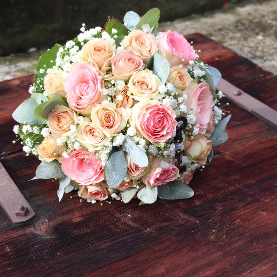 Ein Blumenstrauß aus rosa und gelben Rosen mit Babys Atem und grünen Blättern auf einem Holztisch.