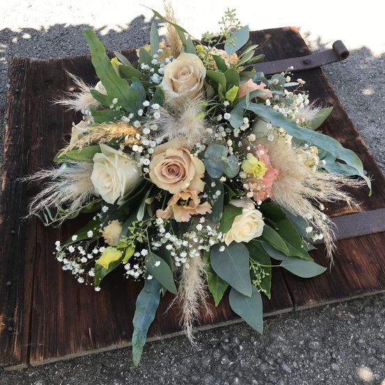 Ein Blumenstrauß aus weißen und rosa Rosen mit Babys Atem und Grün auf einem Holztablett.