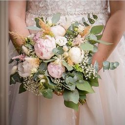 Eine Braut hält einen Hochzeitsstrauß mit rosa und weißen Blumen, grünen Blättern und Babys Atem.