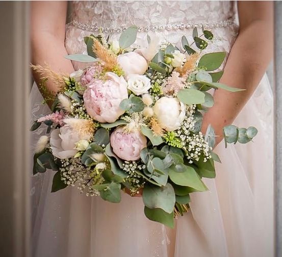 Eine Braut hält einen Hochzeitsstrauß mit rosa und weißen Blumen, grünen Blättern und Babys Atem.