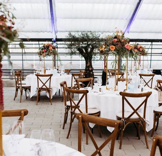 Ein Hochzeitsempfangsbereich mit Tischen und Stühlen für eine Veranstaltung. Blumen-Mittelstücke und elegante Dekoration zieren die Tische.