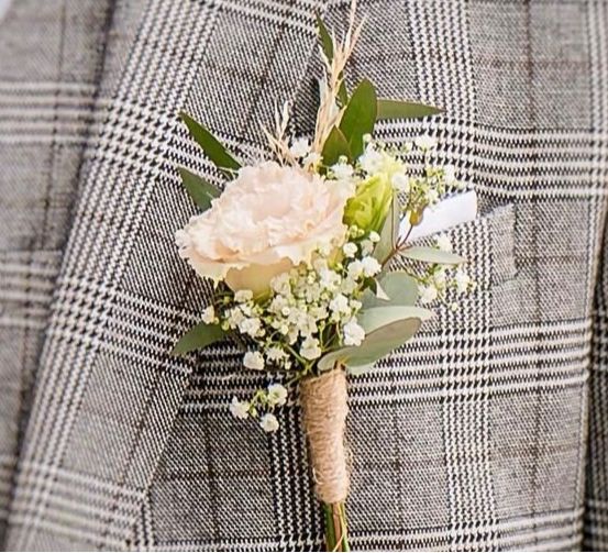 Ein graues Herren-Sakko mit kariertem Muster und einer Blumenboutonnière, die am Revers angesteckt ist. Die Boutonnière enthält eine rosa Rose und Babys atem.