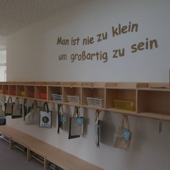 Ein Raum mit einer Holzbank und Regalen, die Taschen und Körbe halten. Ein motivierendes Zitat ist an der Wand gemalt.