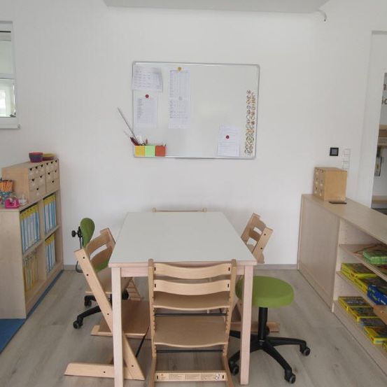 Ein kleiner Lernraum mit Tisch und Stühlen, einem Regal und einer Pinnwand. Links befindet sich ein Spiegel und ein Sofa auf dem Boden.