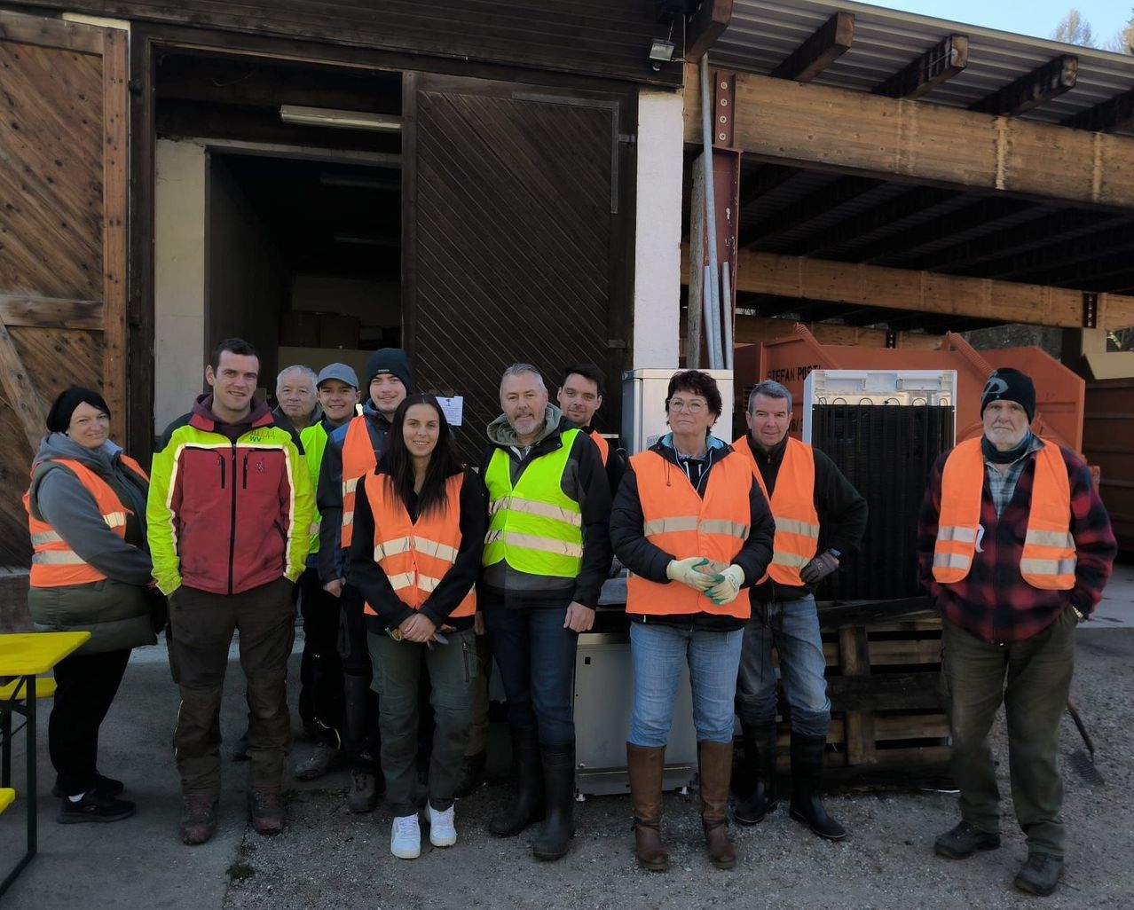 Eine Gruppe von Menschen in orange Warnwesten posiert für ein Foto vor einem Gebäude mit einer Holztür.