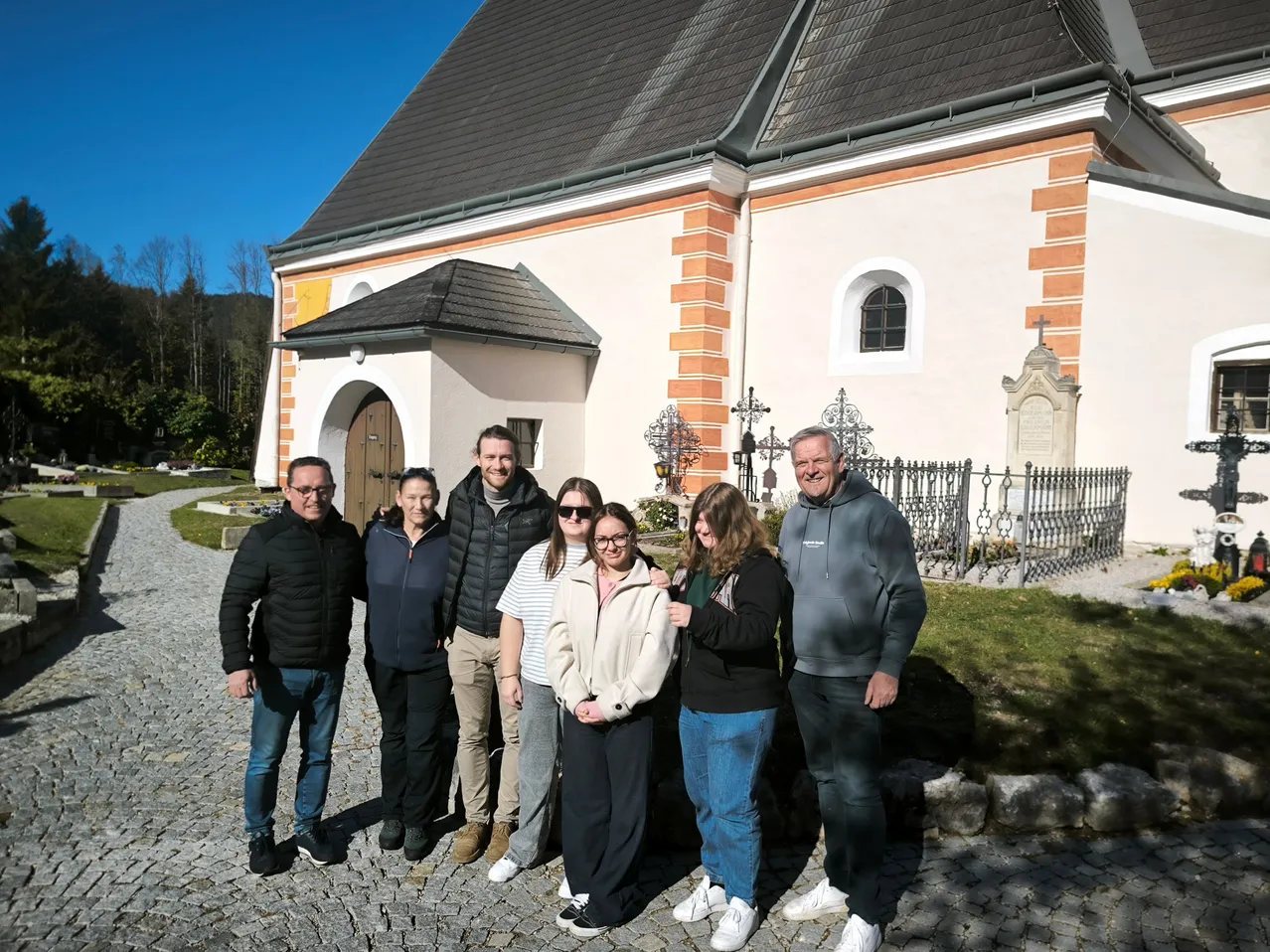 Eine Gruppe von Menschen steht an einem sonnigen Tag vor einer Kirche.