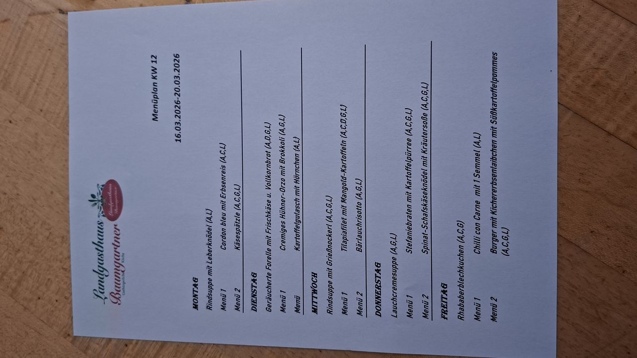Das Bild zeigt ein Wochenmenü mit den Wochentagen und aufgeführten Speisen. Es enthält Einträge wie Rindsuppe, Käseplatte, Cremeschnitte und mehr. Das Menü ist vom 16.03.2026 datiert.