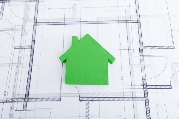 Ein grünes Papierhausmodell liegt auf einem detaillierten Architekturplan und zeigt seine Abmessungen und Anordnung.