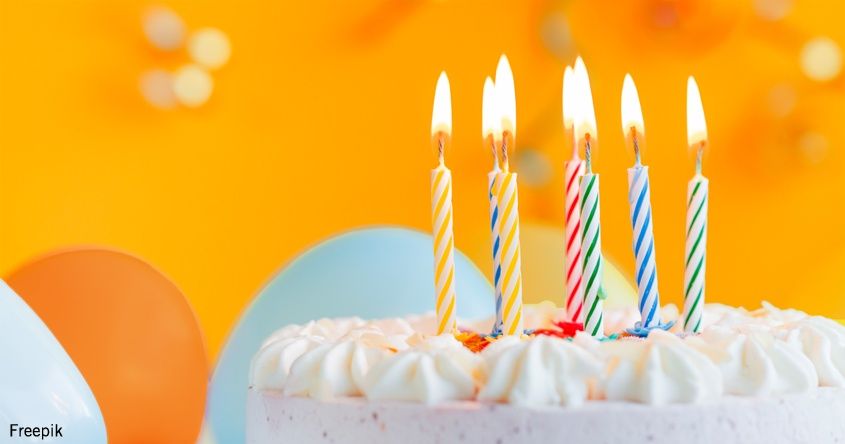 Ein Geburtstagskuchen mit fünf bunten Kerzen ist bereit zum Ausblasen. Der Kuchen hat weiße Glasur mit Streuseln. Der Hintergrund ist ein leuchtendes Orange.