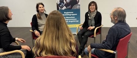 Gruppe von Menschen im Kreis, die diskutieren. Eine Frau mit Brille spricht. Hinter ihnen steht ein Banner, das pro hormon lautet.