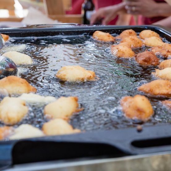 Eine Nahaufnahme einer Frittierpfanne mit sprudelndem Öl und goldbraunen Donuts, die frittiert werden.