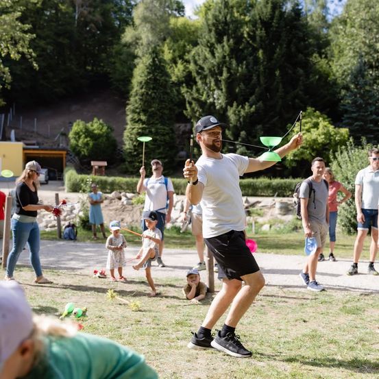 Eine Gruppe von Menschen spielt mit grünen Frisbees in einem Park. Ein Mann balanciert einen Frisbee auf einem Stock.