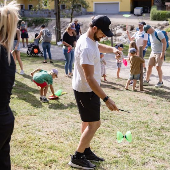 Ein Mann in einem weißen T-Shirt und einer schwarzen Kappe zeigt einem Kind in einem grünen Shirt, wie man einen Frisbee benutzt.