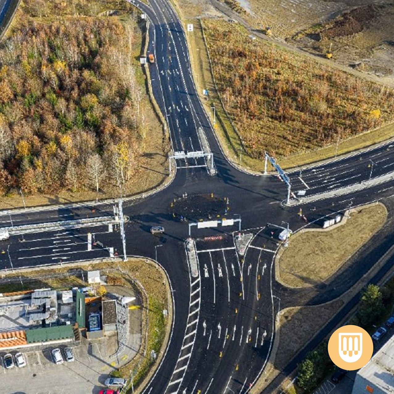 Ein Blick von oben auf eine neu gebaute Kreuzung mit Fahrzeugen, die sie umfahren. Mehrere Autos sind am Straßenrand geparkt.