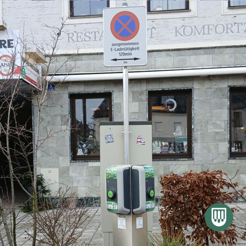 Eine Ladestation für Elektrofahrzeuge steht vor einem Gebäude mit einem Schild, das eine 120-minütige Parkverbotszone anzeigt.