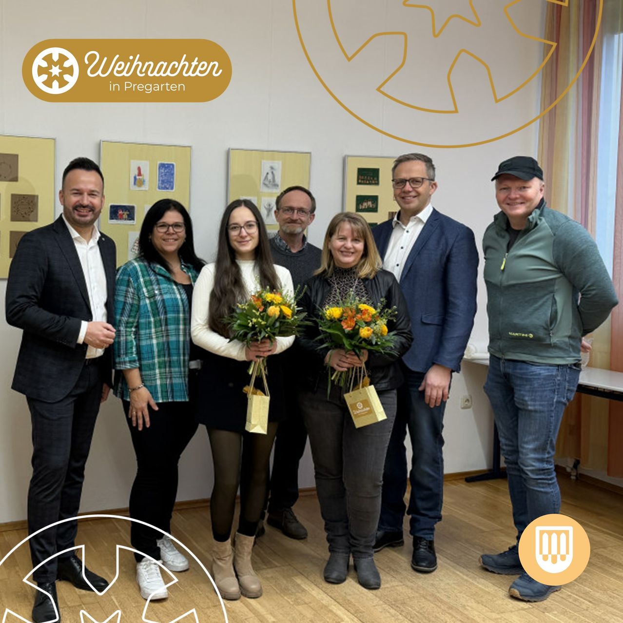 Eine Gruppe von Menschen, möglicherweise eine Familie, steht in einem Raum mit Holzboden, lächelt und posiert für ein Foto. Zwei Frauen halten Blumensträuße, während andere dahinter stehen. Der Raum hat gelbe Wände mit gerahmten Bildern.