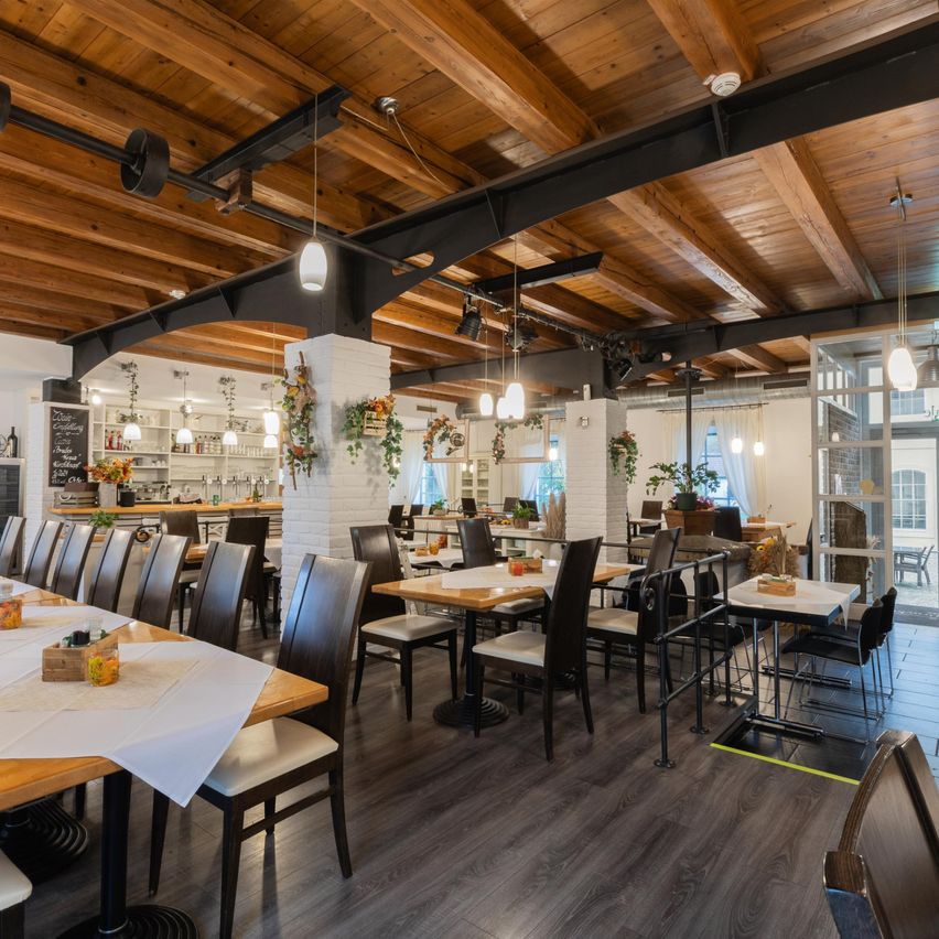 An empty restaurant with wooden tables and chairs, wooden floors, and a wooden ceiling. There are several pendant lights hanging from the ceiling.