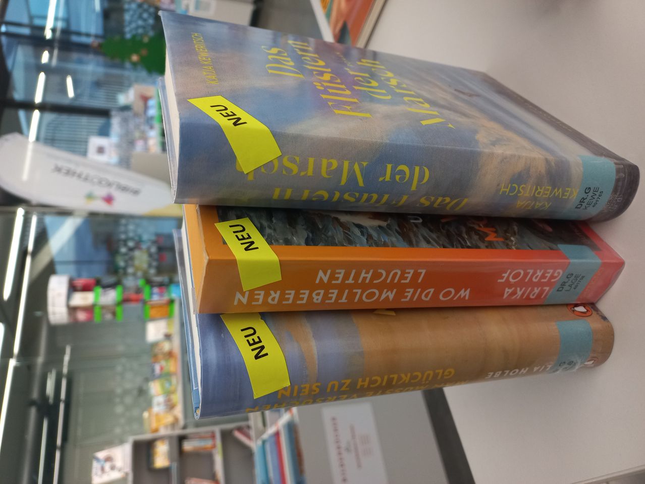 Three books stacked on a shelf, two with yellow labels reading 'NEW', the top book titled 'The Last Letter from Your Lover', the middle one 'The Forgotten Garden', and the bottom one 'The Nightingale'.
