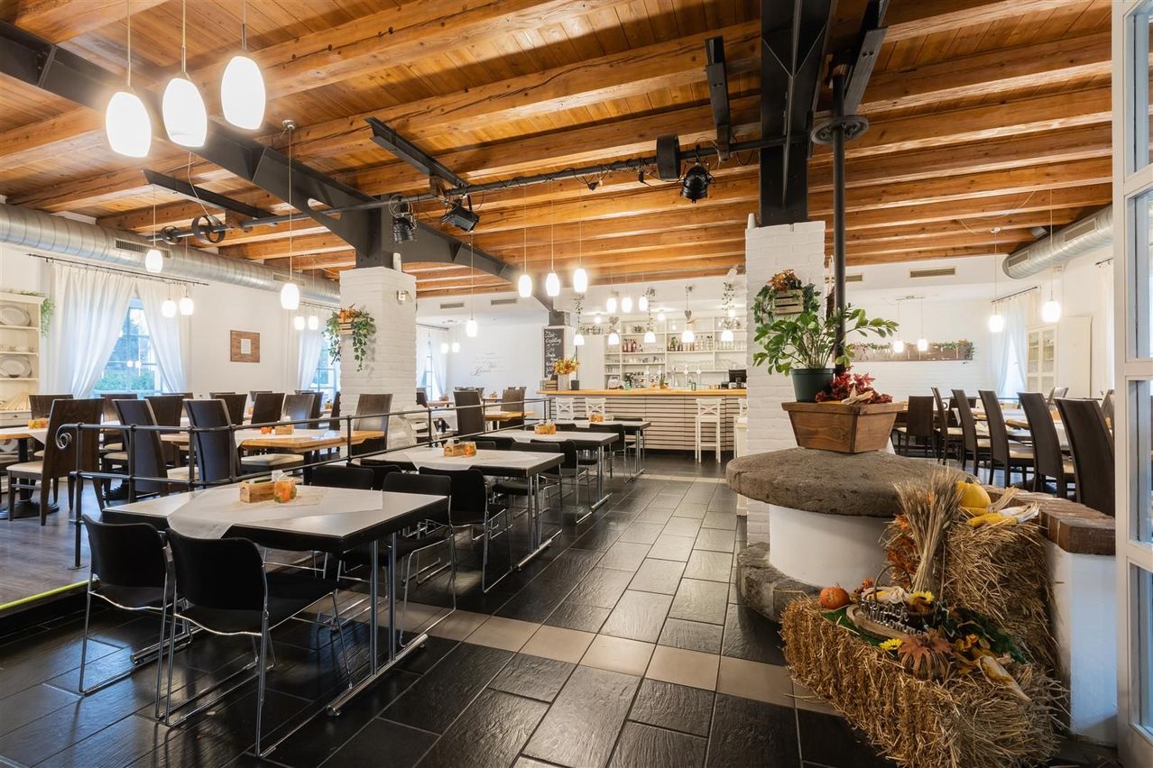 Ein Restaurant mit Holzdecke und schwarzem Fliesenboden. Tische und Stühle sind mit Essen besetzt. Es gibt Pflanzen und Blumen in der Umgebung.