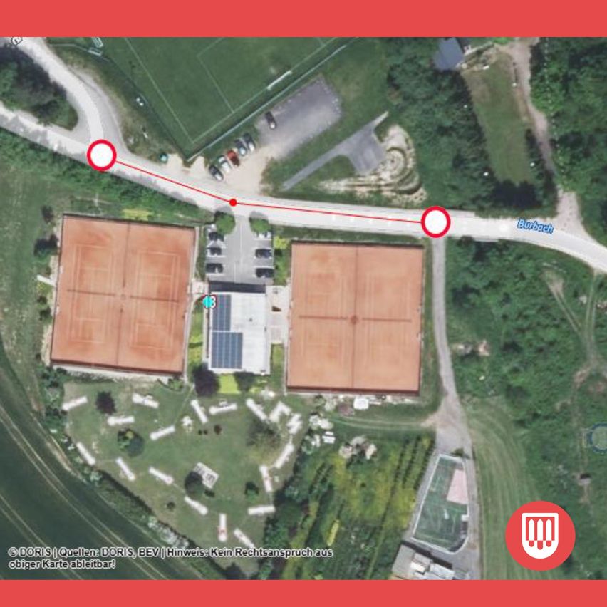 An aerial view of a sports complex with two tennis courts, a parking area, and a pathway. The area is surrounded by greenery and has a red line indicating a route.