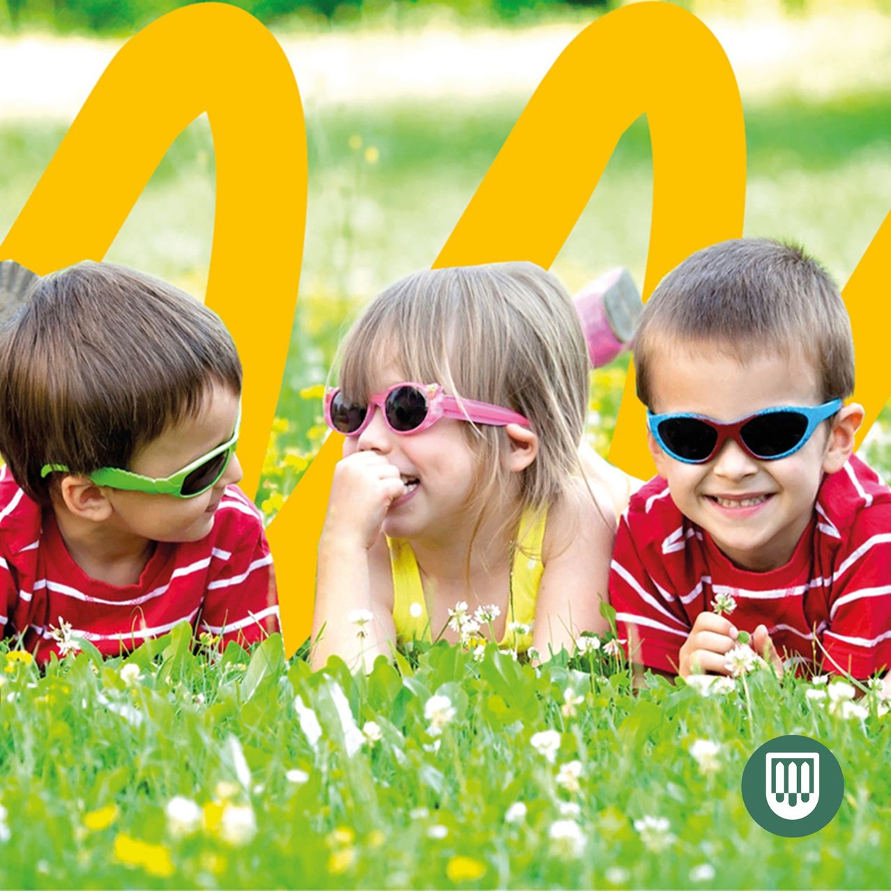 Drei Kinder in bunten Sonnenbrillen liegen auf dem Gras. Das Mädchen in der Mitte hat die Hand am Kinn. Sie scheinen für ein Foto zu posieren.