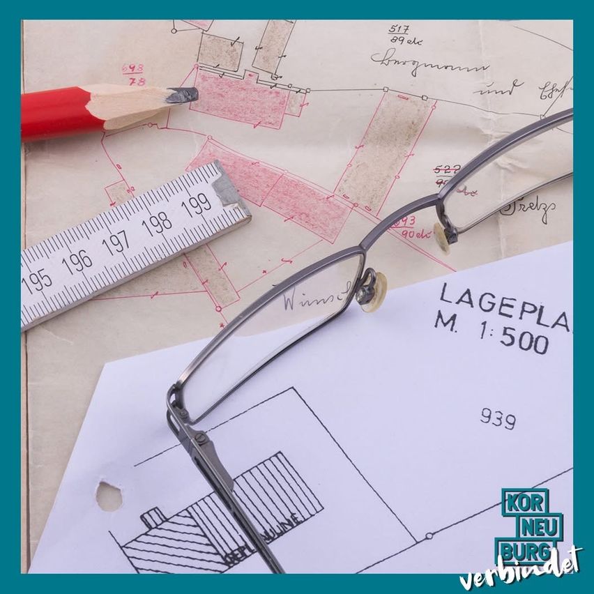 Baupläne mit einem Bleistift, einem Lineal und einer Brille. Das Lineal zeigt von 195 bis 199. Die Papiere zeigen architektonische Pläne. Ein Papier zeigt 'LAGEPLA M. 1:500' und '939'. Der Text 'KOR NEU BURG' ist unten.