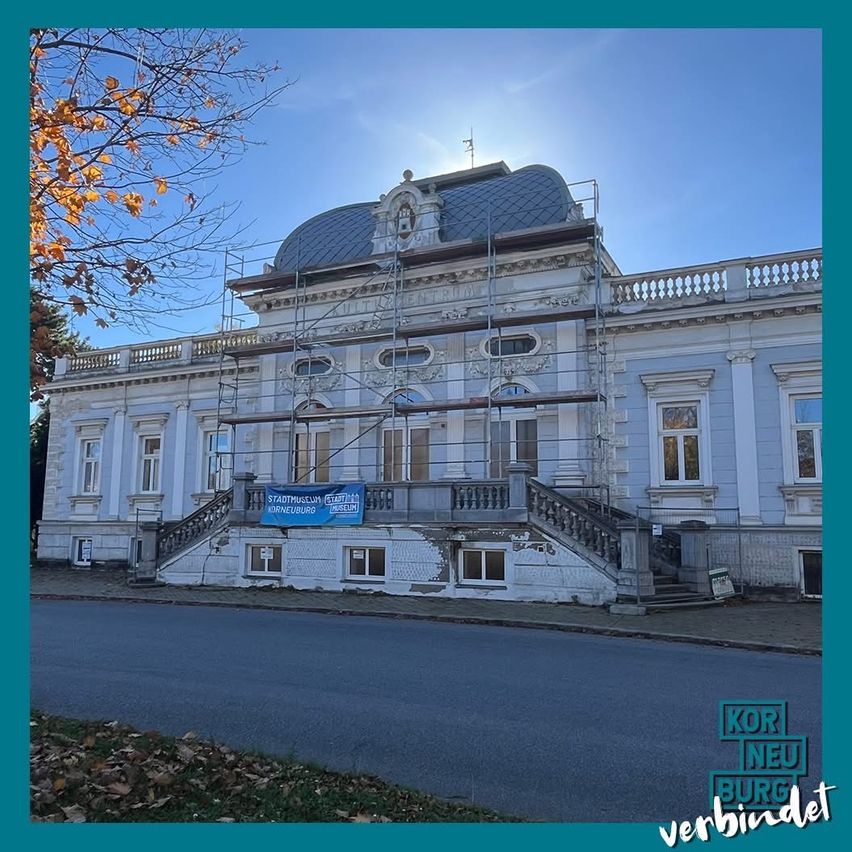 Ein großes, weißes Gebäude mit einem kuppelförmigen Dach ist im Bau. Gerüste umgeben die Struktur. Ein Banner hängt von der Treppe ab.