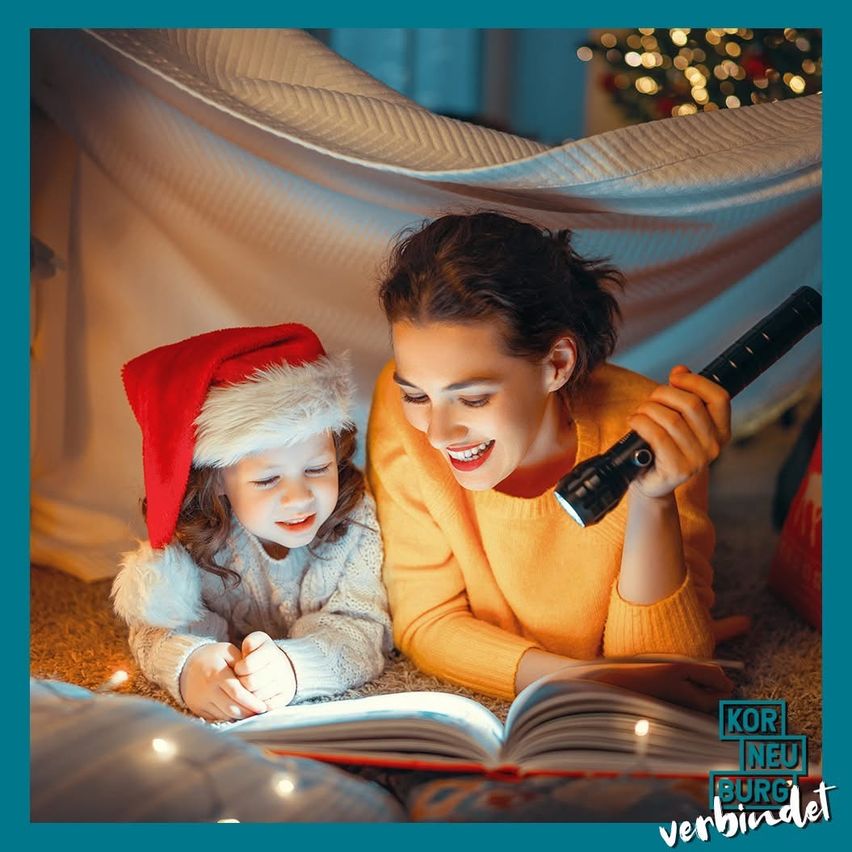 Eine Frau und ein junges Mädchen lesen gemeinsam ein Buch unter einem Zelt, beleuchtet von einer Taschenlampe. Das Mädchen trägt eine Weihnachtsmütze.